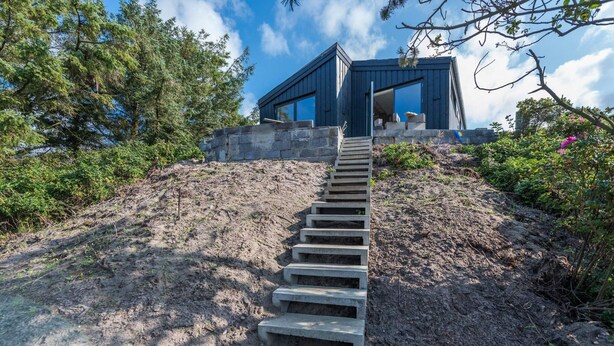 Un edificio moderno con una escalera que lo lleva, rodeado de árboles y arbustos.