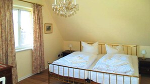 Une chambre à coucher avec un lit double, un lustre, une fenêtre avec des rideaux et une table de chevet.