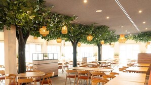 A restaurant with round tables and chairs, indoor plants, and hanging lights. - Beech Resort Boltenhagen (Boltenhagen)