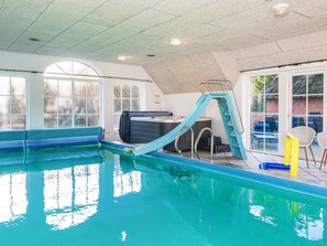 En indendørs swimmingpool med rutsjebane, et spabad og en patio med stole.