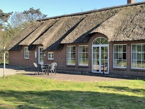 A thatched-roof building with brick walls, a large arched window, and a patio with chairs.