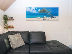 Un soggiorno moderno con un divano in pelle nera, un quadro appeso che raffigura una spiaggia e una piccola pianta su uno scaffale.