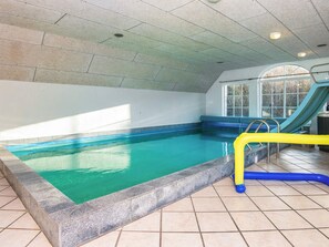 An indoor swimming pool with a blue and yellow pool ladder, a window with a view of trees, and a tiled floor.