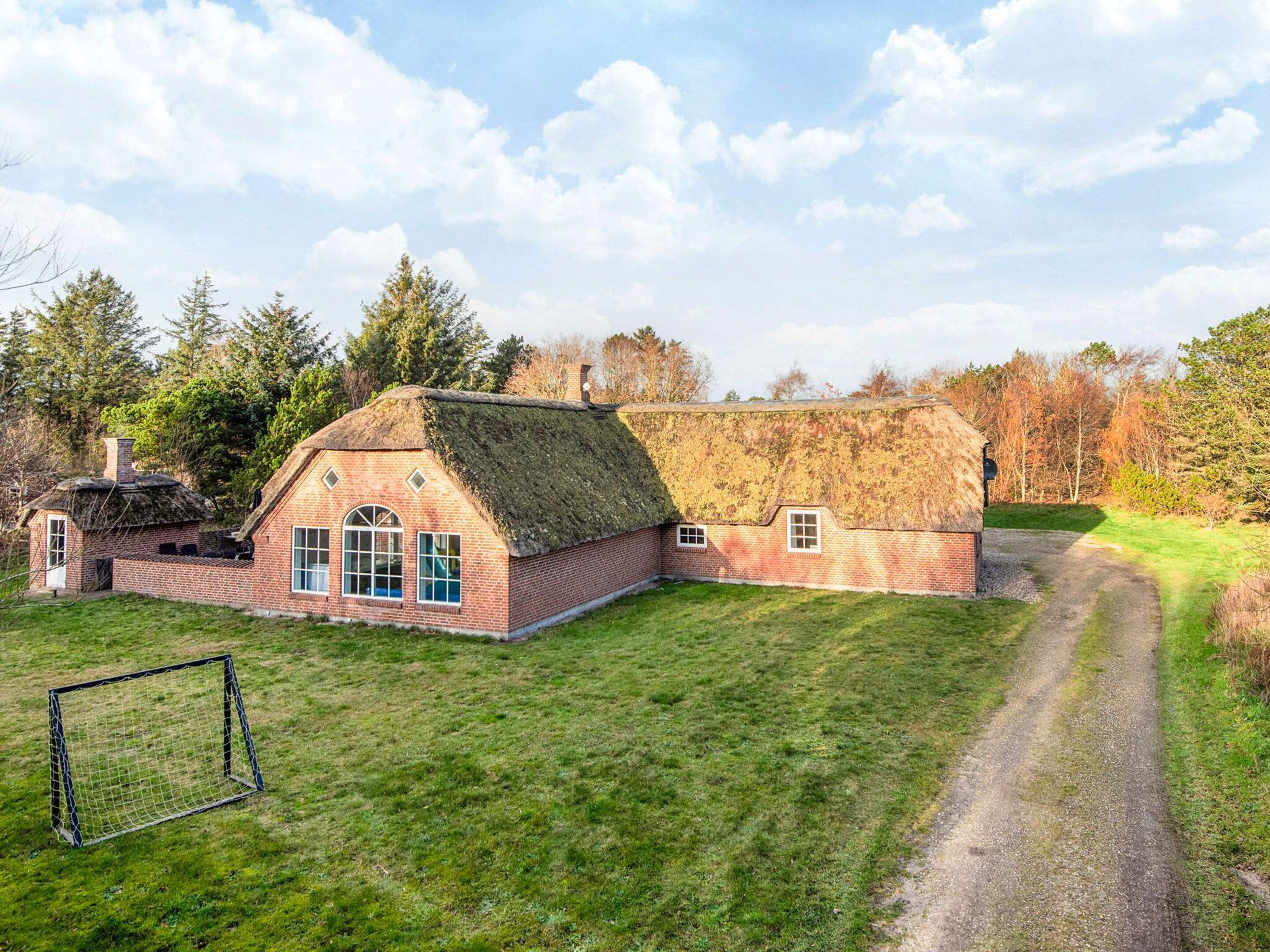 A traditional brick house with a thatched roof, a small attached structure, and a grassy yard with a gravel path.
