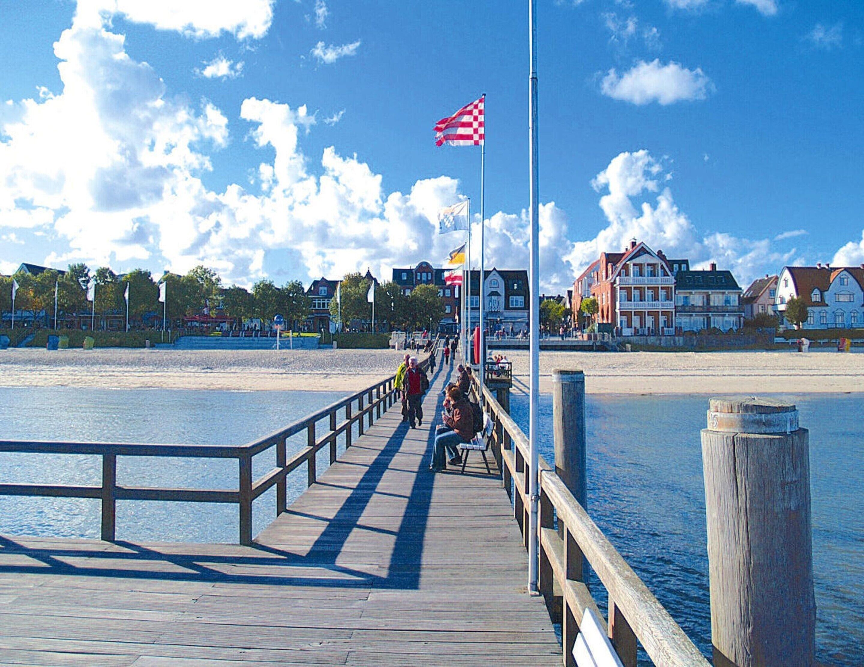 A wooden pier extending into a body of water with a clear sky and buildings in the background.