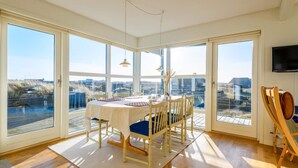 A dining area with a table set for four, large windows, and a flat-screen TV mounted on the wall. - 6 Person Holiday Home in Fano (Fano)