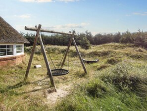 A rustic wooden swing set with a tire swing, a thatched-roof building, and a grassy field. - 4 Star Holiday Home in Harboore (Harboore)