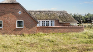 A brick house with a thatched roof and white-framed windows.