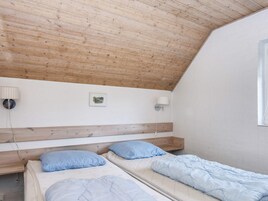 A room with a sloped ceiling, two beds with blue bedding, a wooden headboard, a wall-mounted lamp, and a small framed picture.