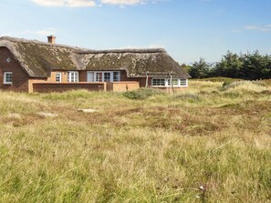 A traditional thatched-roof house with a brick exterior, set in a grassy field with a clear sky. - 4 Star Holiday Home in Harboore (Harboore)