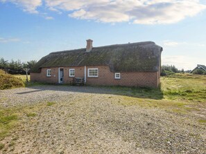 A traditional thatched-roof house with a gravel driveway and a small table outside. - 4 Star Holiday Home in Harboore (Harboore)