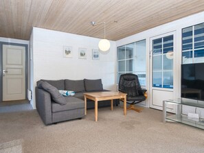 A modern living room with a grey sofa, a wooden coffee table, a black leather chair, and a glass TV stand. - 4 Star Holiday Home in Harboore (Harboore)