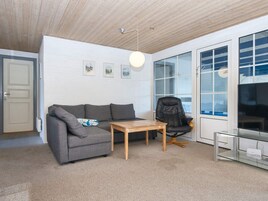 Una sala de estar moderna con un sofá gris, una mesa de centro de madera, un sillón de cuero negro y un mueble de televisión de vidrio.
