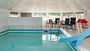 An indoor swimming pool with a slide, surrounded by chairs and tables.