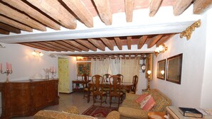Ein gemütliches Wohnzimmer mit Holzbalkendecke, einer Essecke mit Tisch und Stühlen sowie einem Sofa mit gemustertem Bezug.