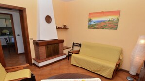A living room with a fireplace, a sofa, a dining table with a vase of flowers, and a painting on the wall. - Holiday Home in Lucca With Pool & Garden (Capannori)