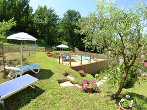 Ein Garten mit einer Holzterrasse, einem Schwimmbecken, Liegestühlen und Kübelpflanzen.