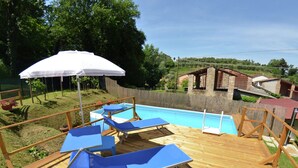 A wooden deck with a pool, blue lounge chairs, and a white umbrella. - Holiday Home in Lucca With Pool & Garden (Capannori)