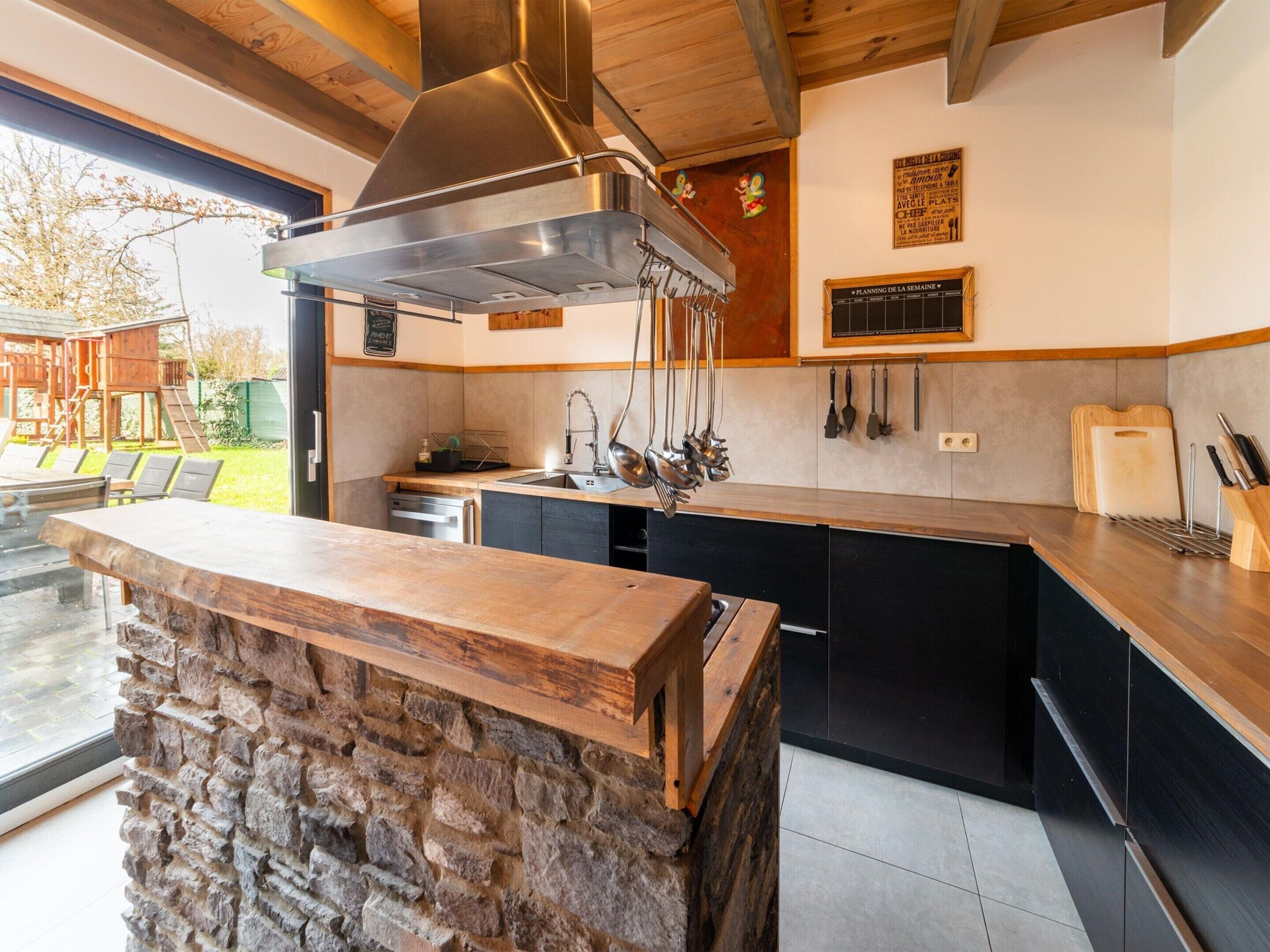 Une cuisine moderne dotée d’un îlot en pierre, d’une hotte en acier inoxydable et de meubles de rangement noirs.