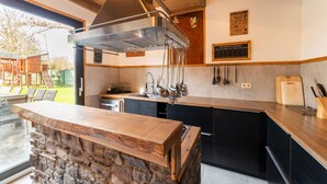 Une cuisine moderne dotée d’un îlot en pierre, d’une hotte en acier inoxydable et de meubles de rangement noirs.