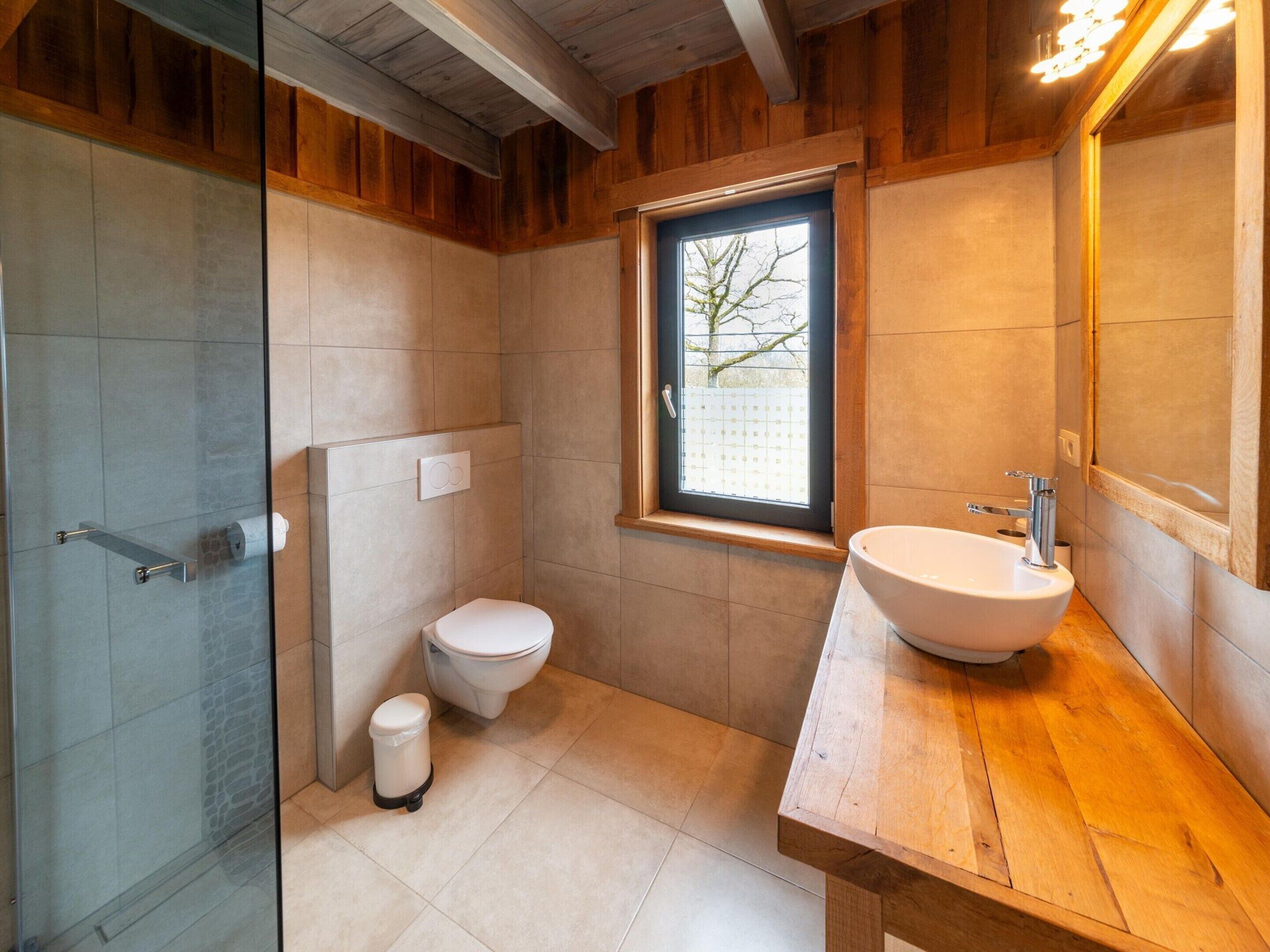 A bathroom with a glass shower enclosure, a toilet, and a sink with a wooden countertop.