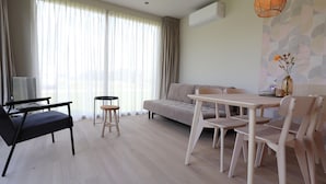 Ett modernt vardagsrum med en soffa, ett matbord med stolar, en tv och ett stort fönster med gardiner.