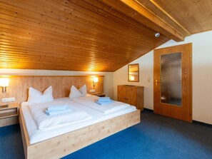 Eine Holzbalkendecke, ein Bett mit weißer Bettwäsche, ein Nachttisch, ein Holzkasten und eine Milchglasschürze.