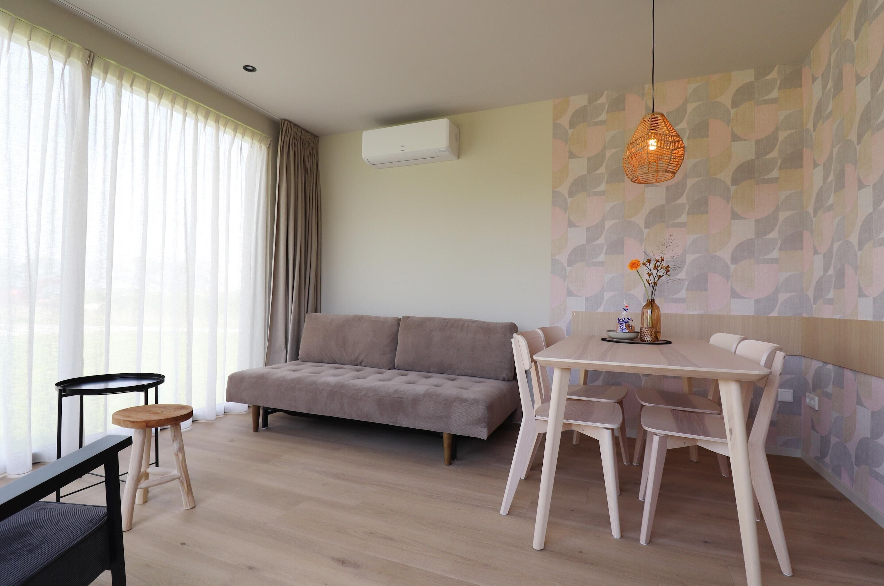 Una sala de estar moderna con sofá, mesa de comedor, sillas y una lámpara colgante.