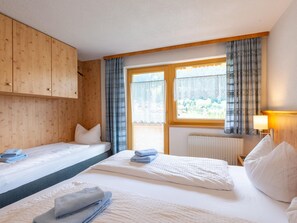 Ein Zimmer mit zwei Betten, Holzvertäfelung, einem mit Vorhängen versehenen Fenster, einem Heizkörper und einer Lampe.