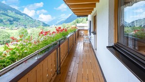 A wooden deck with a metal railing, overlooking a mountainous landscape with red flowers. - Chalet in Gaschurn Near Ski Slopes (Gaschurn)