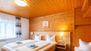 Ein schlicht eingerichtetes Schlafzimmer im Chalet-Stil mit einem großen Bett, Nachttischen und einem Fenster mit Vorhängen.