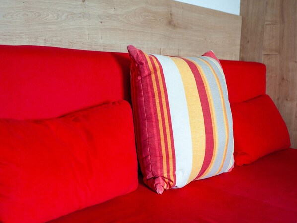 A red sofa with a striped pillow against a wooden wall. - Apartment in Tyrol Near Ski Lift (Uderns)