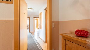 Un couloir avec une porte en bois portant l’inscription « STOCK », qui donne sur une pièce contenant un meuble en bois et un objet rouge posé sur le dessus.