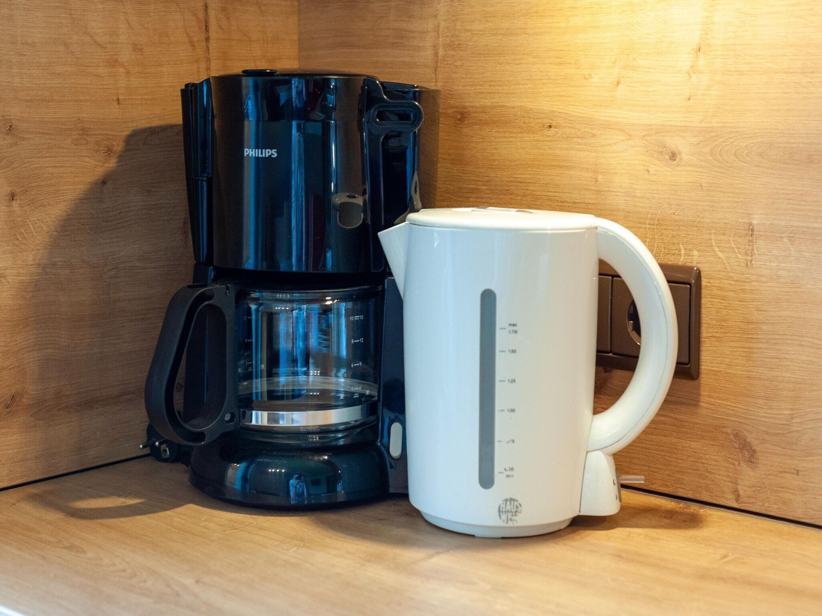A coffee maker and a white mug on a wooden surface.