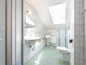 Ein modernes Badezimmer mit Oberlicht, Waschbecken, Toilette und Duschbereich.