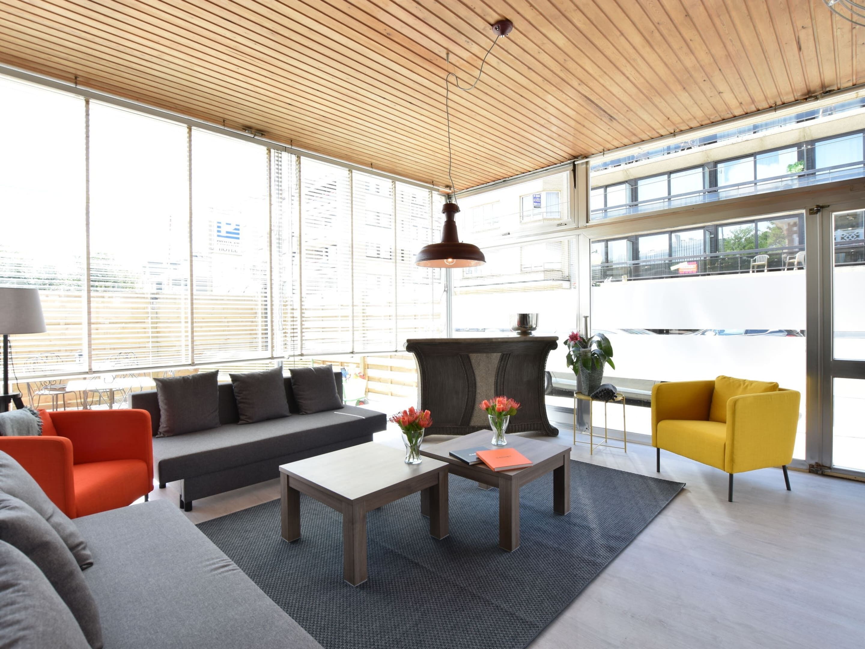 Un interior moderno con techo de madera, ventanas amplias, un sofá, un sillón amarillo y una mesa de centro.