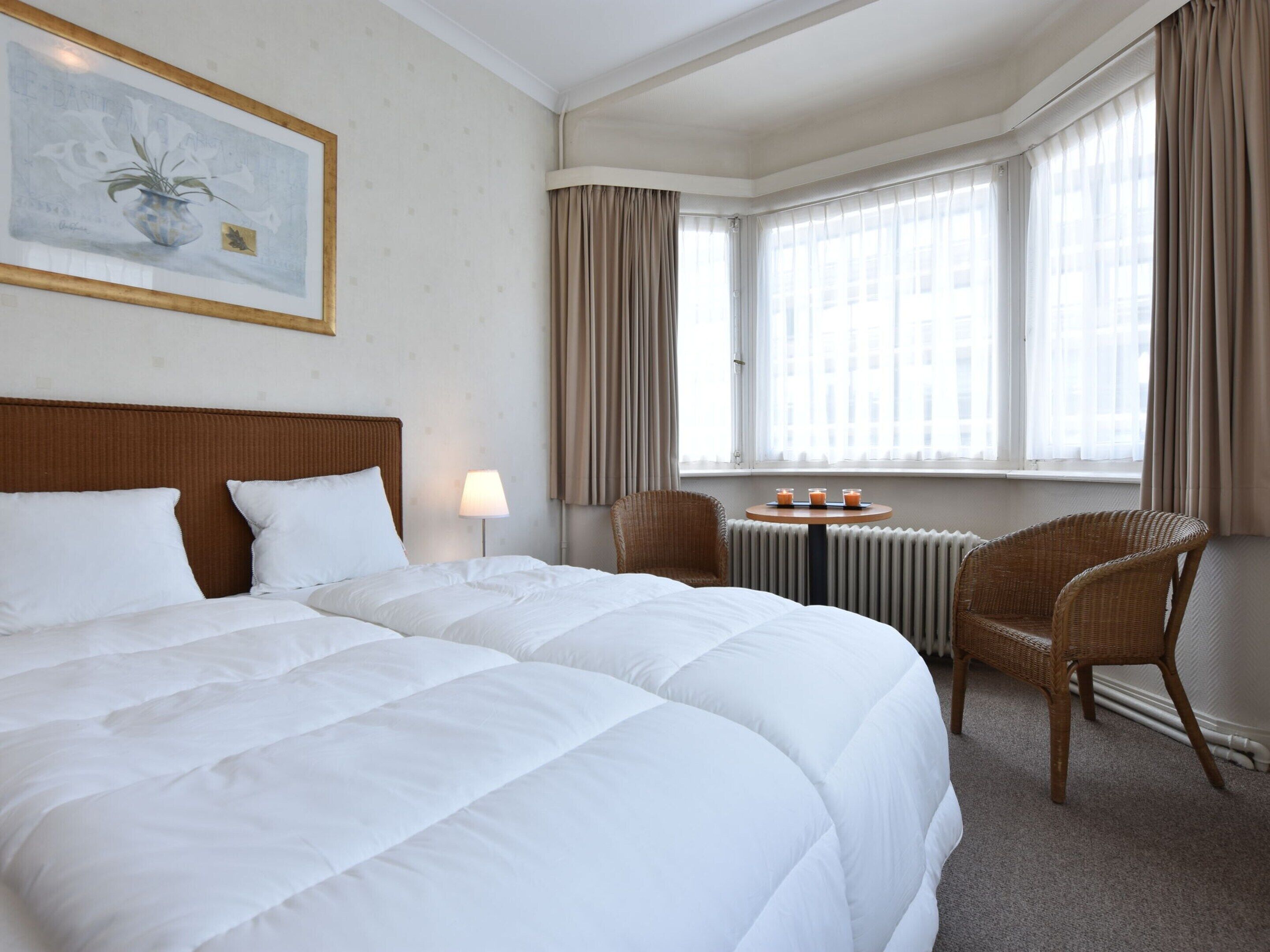 Ein Hotelzimmer mit einem großen Bett, einem kleinen Tisch mit Getränken, einem Sessel und einem Fenster mit Vorhängen.