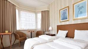 A hotel room with two beds, a small table with a lamp, two chairs, and a window with curtains. - Sun & Sand Group Getaway (De Panne)