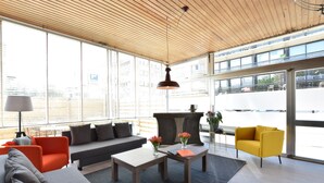A modern interior with a wooden ceiling, large windows, a sofa, a coffee table, and a yellow armchair. - Sun & Sand Group Getaway (De Panne)