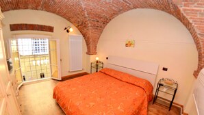 A bedroom with a brick ceiling, a bed with an orange bedspread, a radiator, and a small table with a lamp. - Apartment in the Historic Center of Lucca (Lucca)