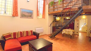 A living room with a red sofa, a small table, and a staircase leading to an upper level. - Apartment in the Historic Center of Lucca (Lucca)