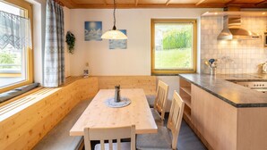 A cozy cabin-style room with a wooden ceiling, a dining table with chairs, a kitchen area with a sink and stove, and a window with curtains. - Spacious Apartment Near the Centre and ski Resort (Gaschurn)