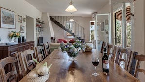 A dining area with a wooden table, chairs, a vase of flowers, a wine bottle, and a glass of wine. - Belvilla by OYO Casale Degli Ulivi (Lucignano)