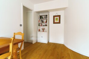 Ein Zimmer mit einem Holzesstisch, Stühlen, einem weißen Bücherregal und einem gerahmten Bild an der Wand.