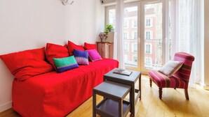 A bright living room with a red sofa, a striped armchair, and a small table. - PARI-PEC534 Summary: (Paris)