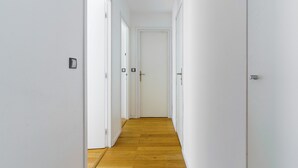 A narrow hallway with white walls and wooden flooring, leading to a closed door at the end. - PARI-PEC534 Summary: (Paris)