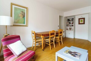 A dining area with a wooden table and chairs, a sofa with a striped cushion, and a framed painting on the wall. - PARI-PEC534 Summary: (Paris)