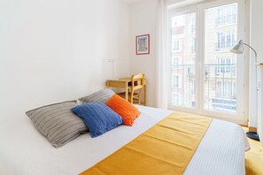 A bedroom with a bed, pillows, a desk, and a window. - PARI-PEC534 Summary: (Paris)