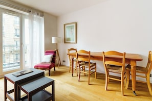 A room with a dining table, chairs, a small sofa, a lamp, and a window with curtains. - PARI-PEC534 Summary: (Paris)