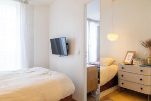 A bedroom with a bed, a dresser, a mirror, a television, and a hanging light fixture. - Beautiful 1BD Apartment in Saint Lazare (Paris)